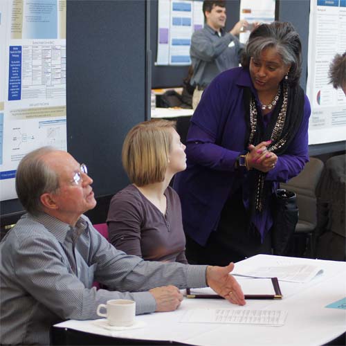 People talking by a poster at research day.