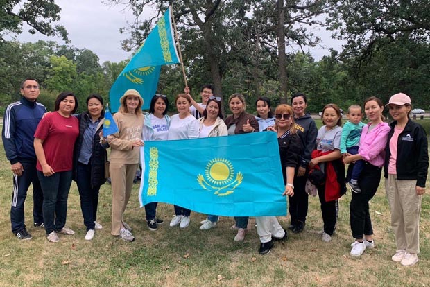 Visiting scholars standing outside holding a large Kazakhstan flag.